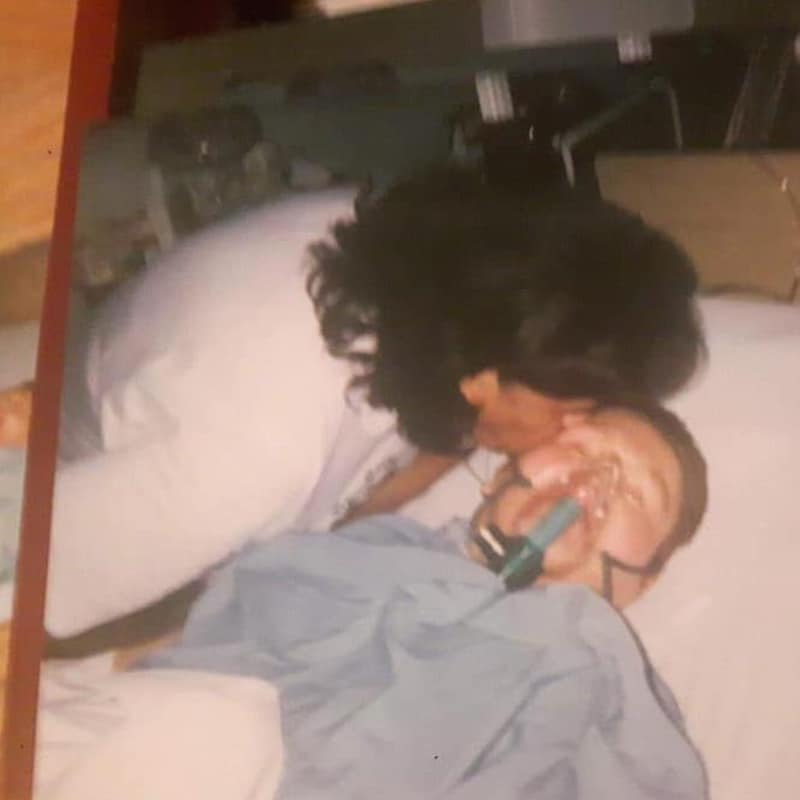 La mère d'Emily l'embrasse sur le front. Emily porte un masque pour l'aider à respirer dans un lit d'hôpital.