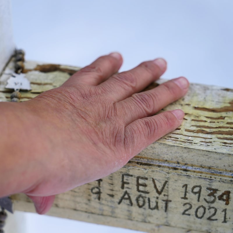 Françoise Ruperthouse pose sa main sur la croix de sa mère au cimetière. Les dates Fév. 1934 et 9 août 2021 sont gravés dans le bois.