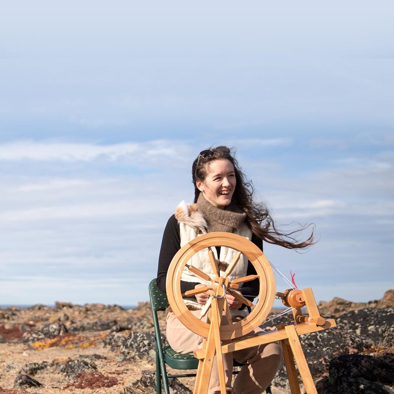 Rachel, derrière son rouet, file de la laine devant une vaste étendue de toundra.