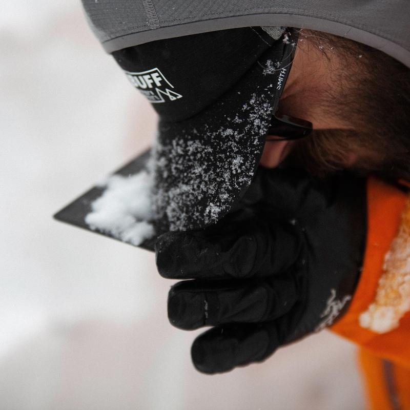 Un homme  en habit d'hiver observe de près une plaquette pour analyser la grosseur des flocons de neige.