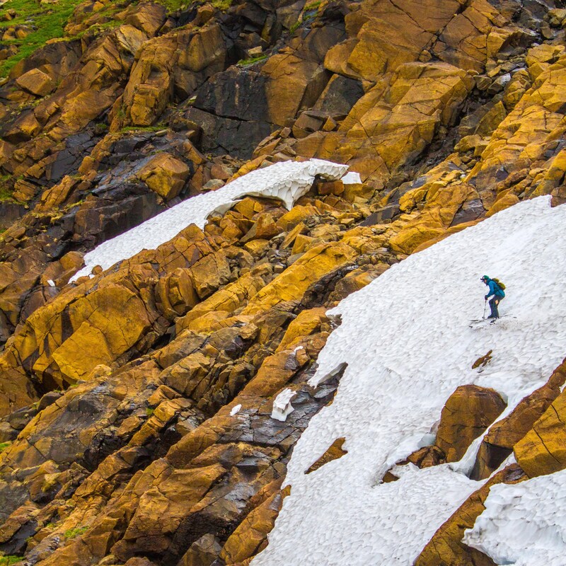 Un skieur alpin descend sur une piste où il reste peu de neige et qui est entourée de rochers.