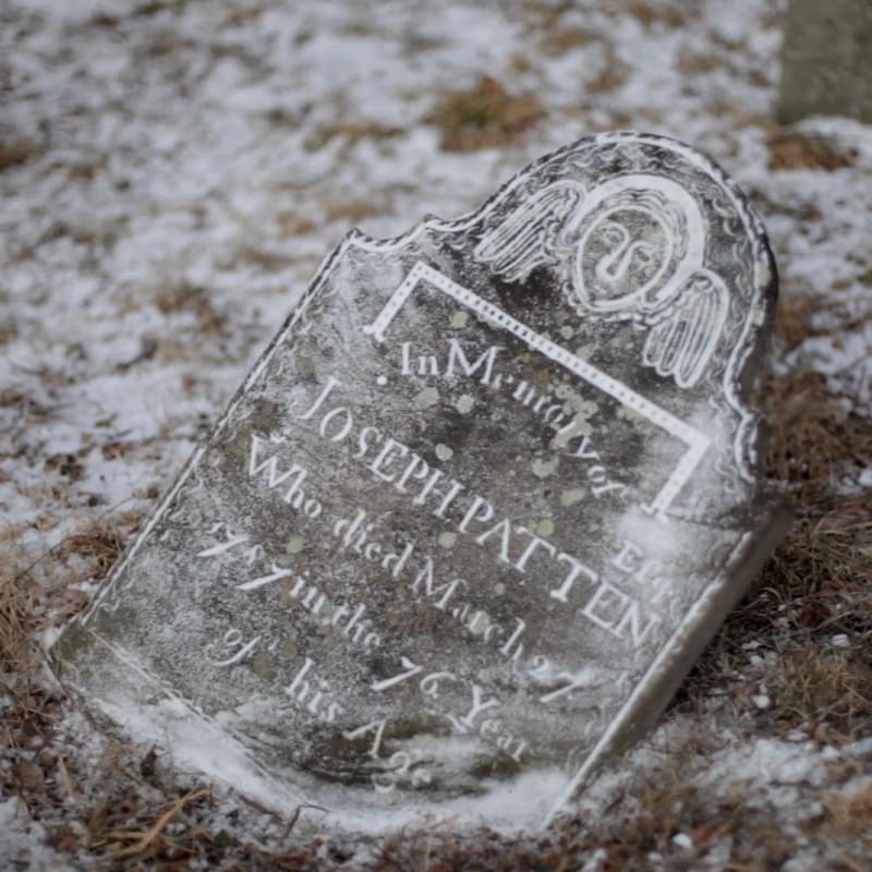 Un pierre tombale sur laquelle de la neige a été appliquée, rendant les inscriptions lisibles.