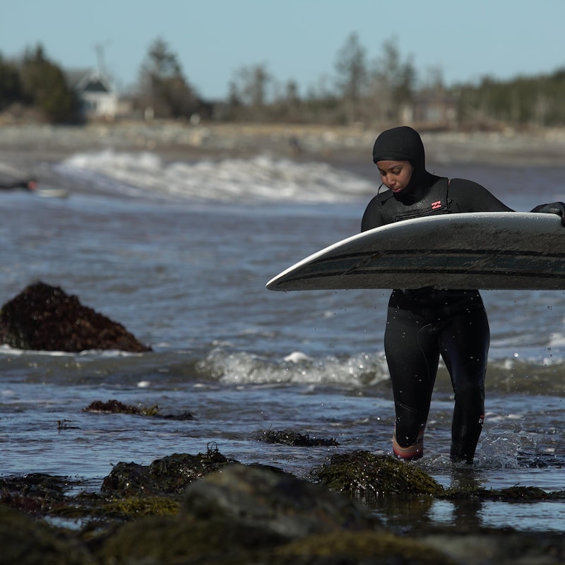Juniper marche avec sa planche de surf sur les berge de l'océan.