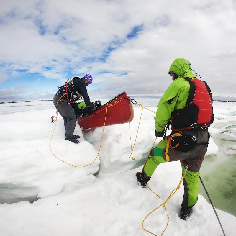 Deux aventuriers tirent et poussent un canot, coincé sur une glace.