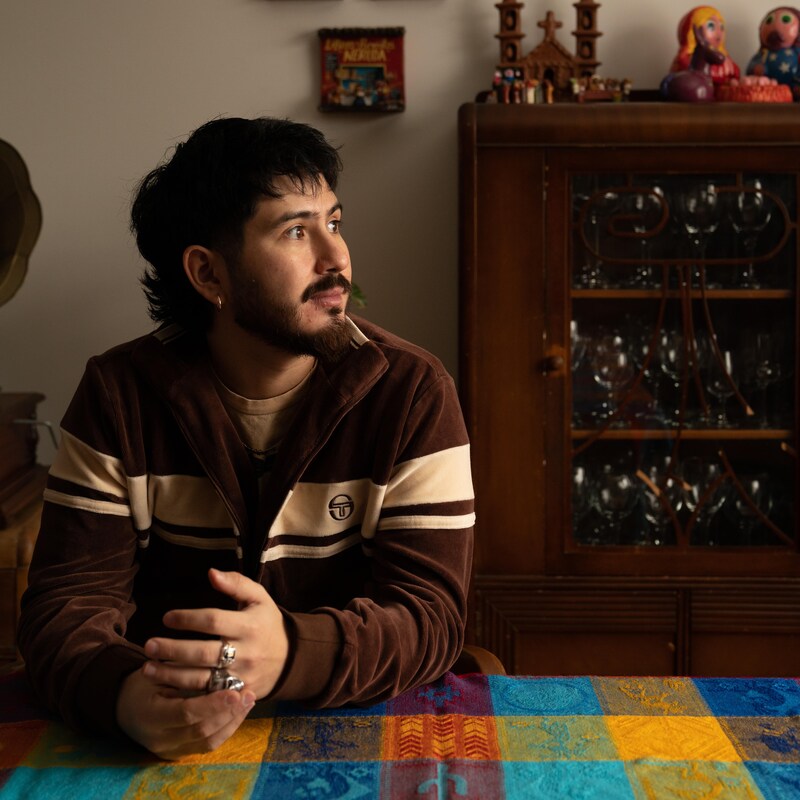 Felipe est assis à la table colorée de la salle à manger de sa mère. Il regarde vers l'extérieur.