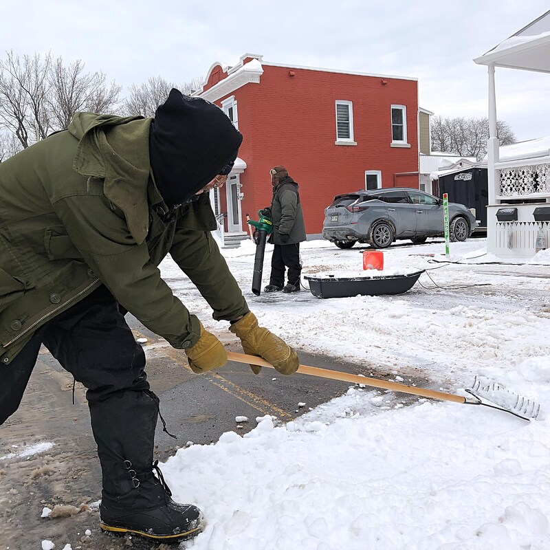Un homme répartit la neige avec un râteau dans la rue du tournage.