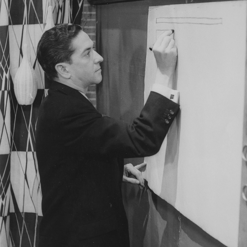 Fernand Seguin écrivant sur un tableau dans le décor de l'émission.