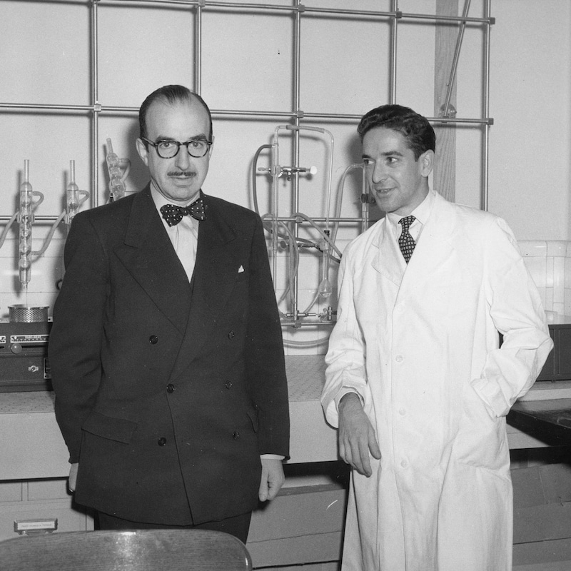 Fernand Seguin en sarrau aux côtés de Paul Dumas dans un laboratoire.