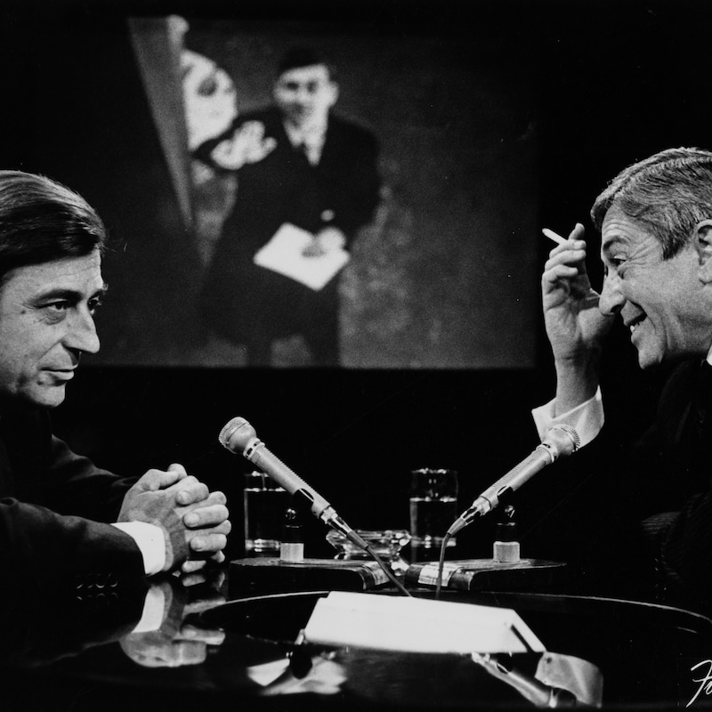 Dans un studio de télévision, François Périer s'entretient avec Fernand Seguin. Une image floue de François Périer, probablement dans un de ses films, est projetée sur le mur du fond.
