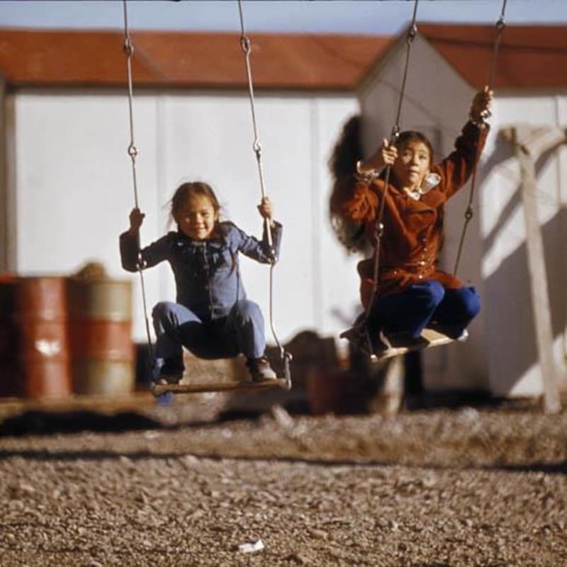 Photo d'archives de deux fillettes accroupies sur des sièges de balançoire.