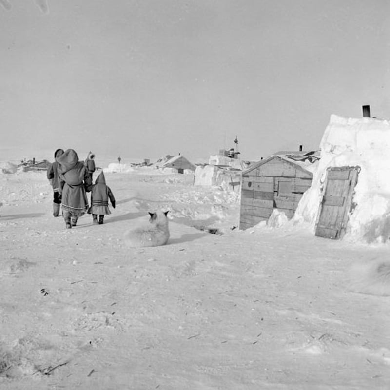 Photo d'archives d'une famille près d'habitations faites de blocs de neige et de planches de bois.
