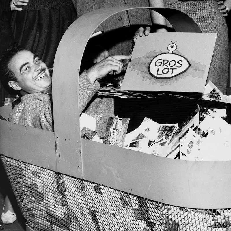 L'annonceur Henri Bergeron assis dans un panier géant contenant le courrier des téléspectateurs.