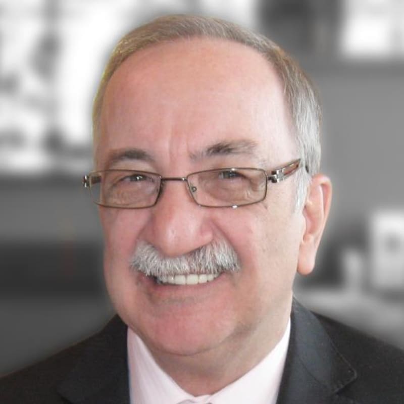 Monsieur Bonneau porte un veston et une cravate. Il a une moustache grise et porte des lunettes.