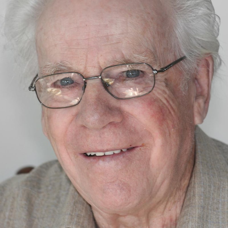 Monsieur Belland regarde l'objectif. Il a les yeux bleus et porte des lunettes.