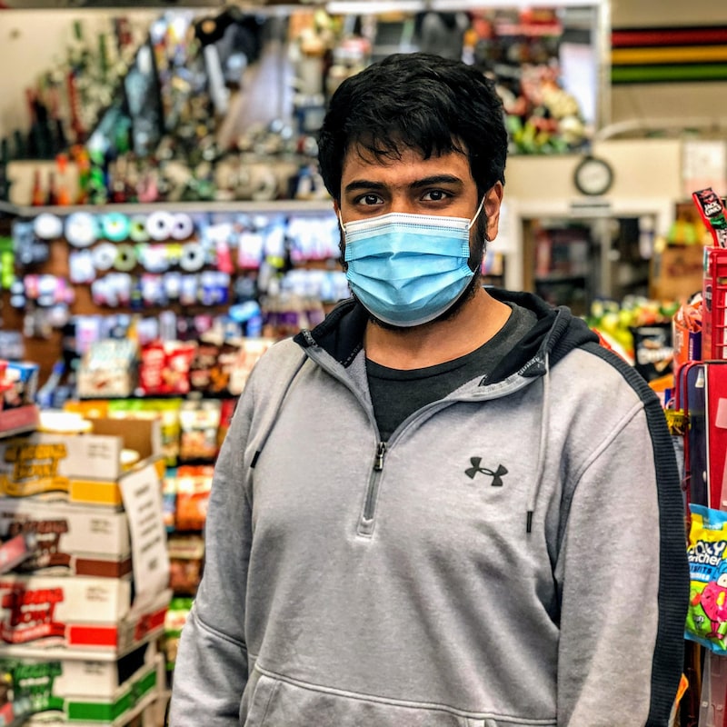 Prana Mago portant un masque debout dans son épicerie.