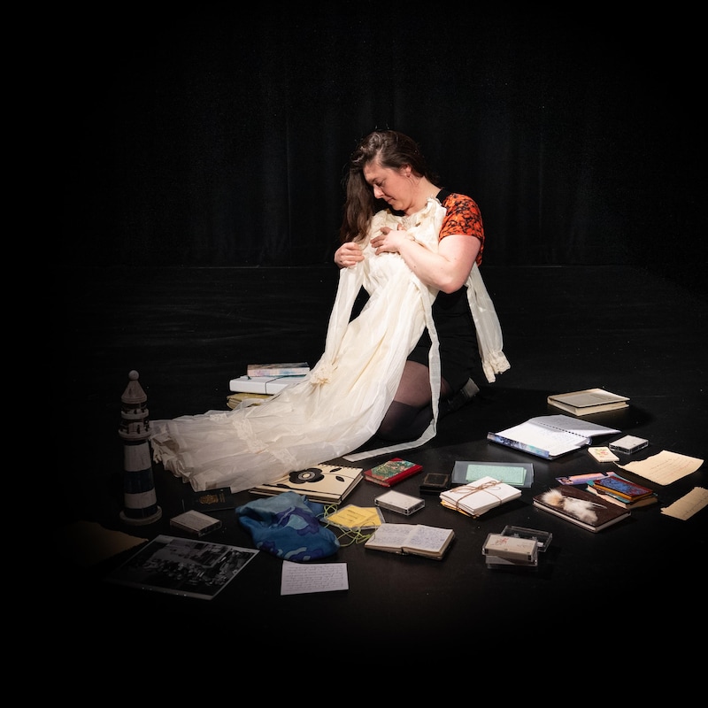 Isabelle Rivest tient la robe de mariage de sa mère. Des cassettes, photos et livres sont étalés sur la scène principale de l’Agora des Arts.