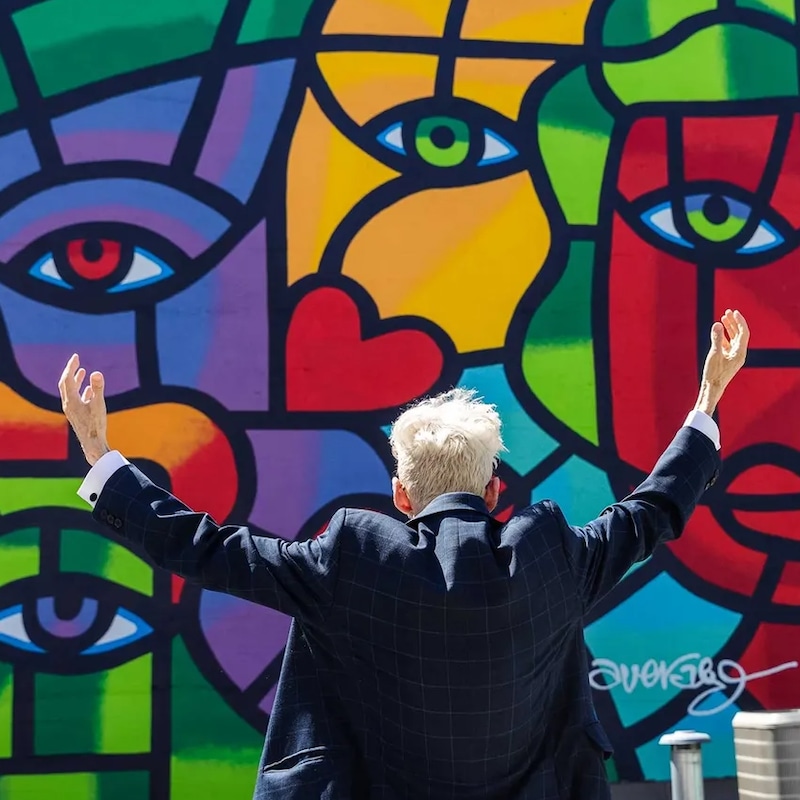 Joe Average, les bras grands ouverts devant sa murale « 40 years later », à Vancouver.