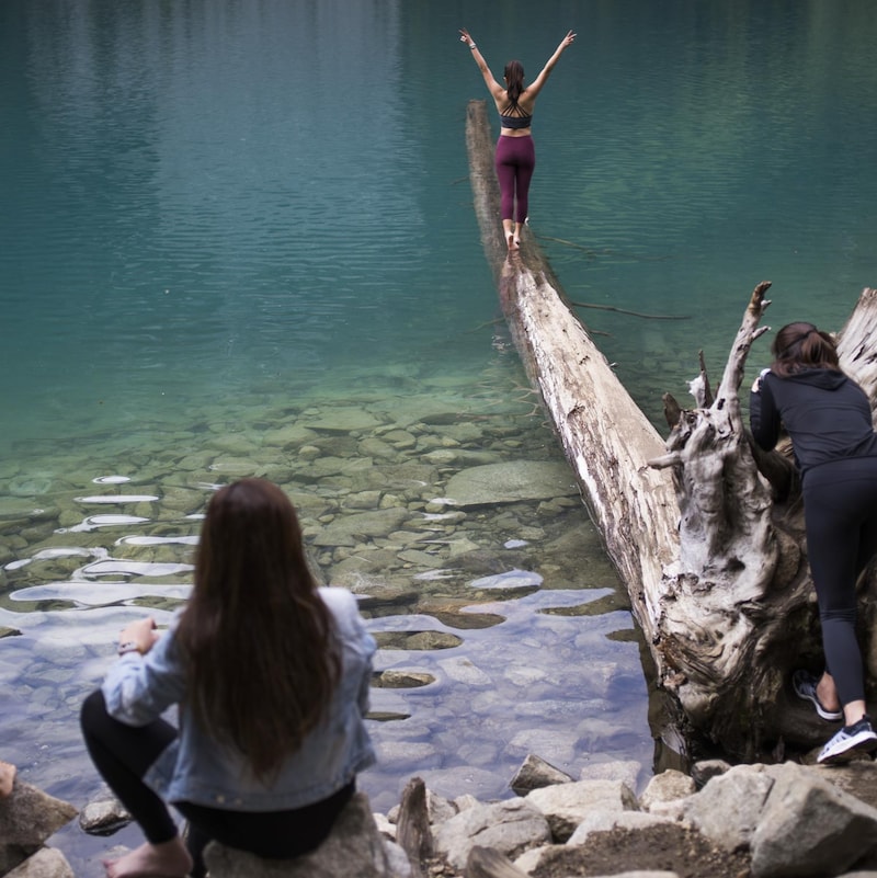 Une jeune femme fait une pose gracieuse sur un tronc à demi-submergé aux abords d'un lac du parc britanno-colombien de Joffre Lakes.