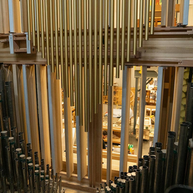 En avant-plan, la photo montre les tuyaux. À travers la façade de l'instrument, on voit les employés travailler dans l'atelier, en contrebas.