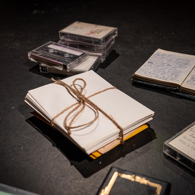 Des lettres, cahiers, et cassettes sont déposés sur une scène.