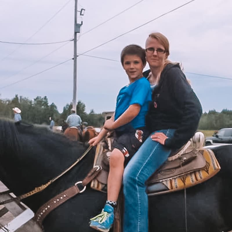 Caroline est sur un cheval, avec son fils devant elle, dans un parking.