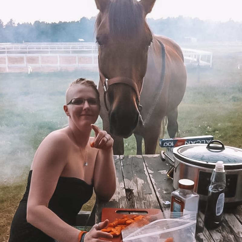 Caroline en train de cuisinier sur une table de pique-nique en bois, avec un cheval derrière elle.