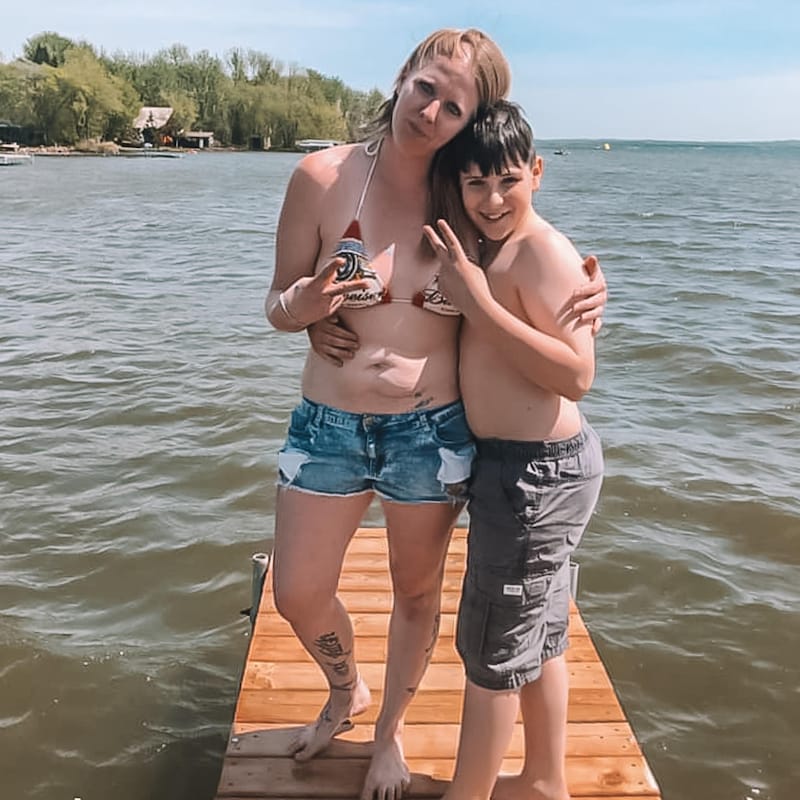 Caroline a le bras autour de son fils, en train de poser en maillot de bain devant la mer.
