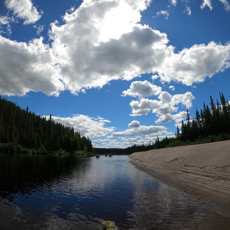 Une rivière bordée de roche et de conifères, en grand angle.
