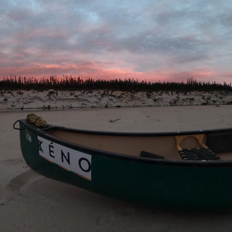 Un canot est déposé sur une plage de sable, au soleil couchant.
