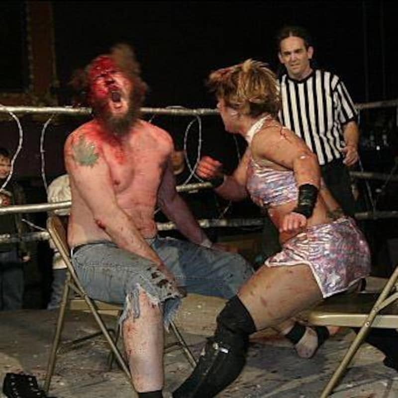 Le lutteur et la lutteuse sont assis sur des chaises et l'homme qui vient de recevoir un coup de poing a le visage couvert de sang.