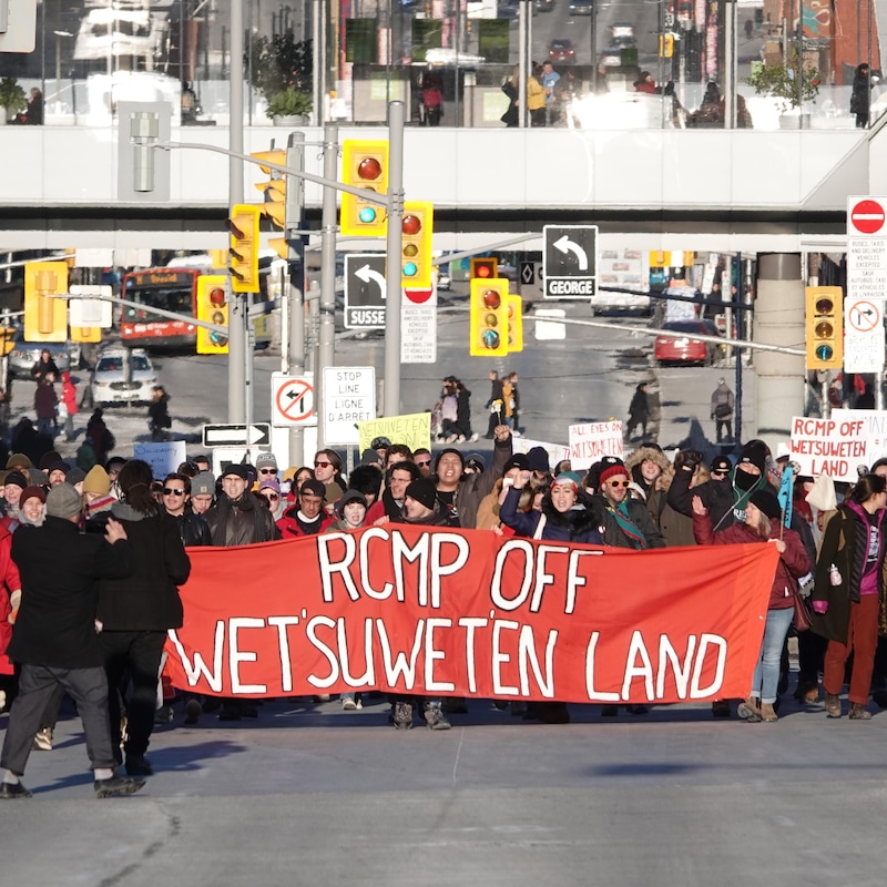 Des manifestants marchant derrière une bannière sur la rue Wellington, à Ottawa, en hiver.