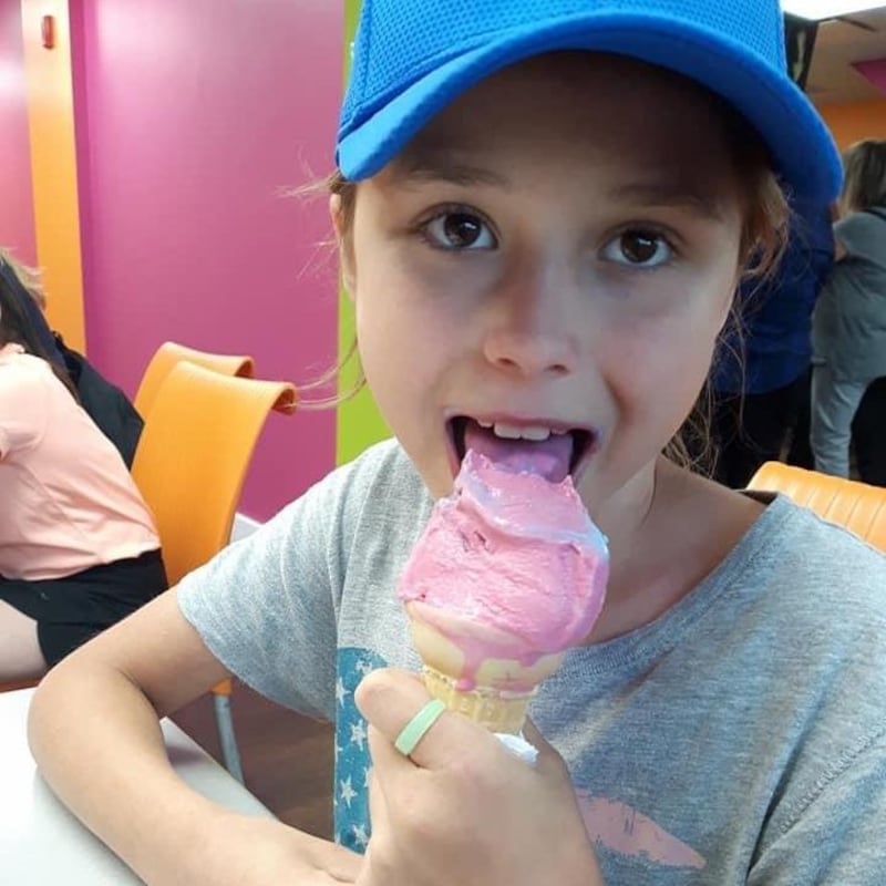 Une fillette porte une casquette bleue et mange une crème glacée.