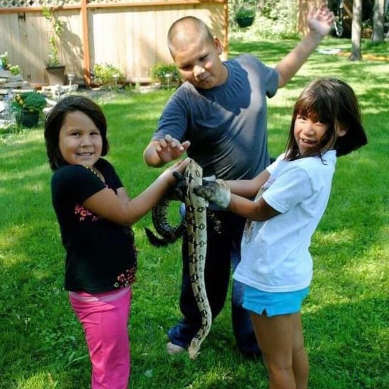 Trois enfants dans un jardin tiennent un serpent.