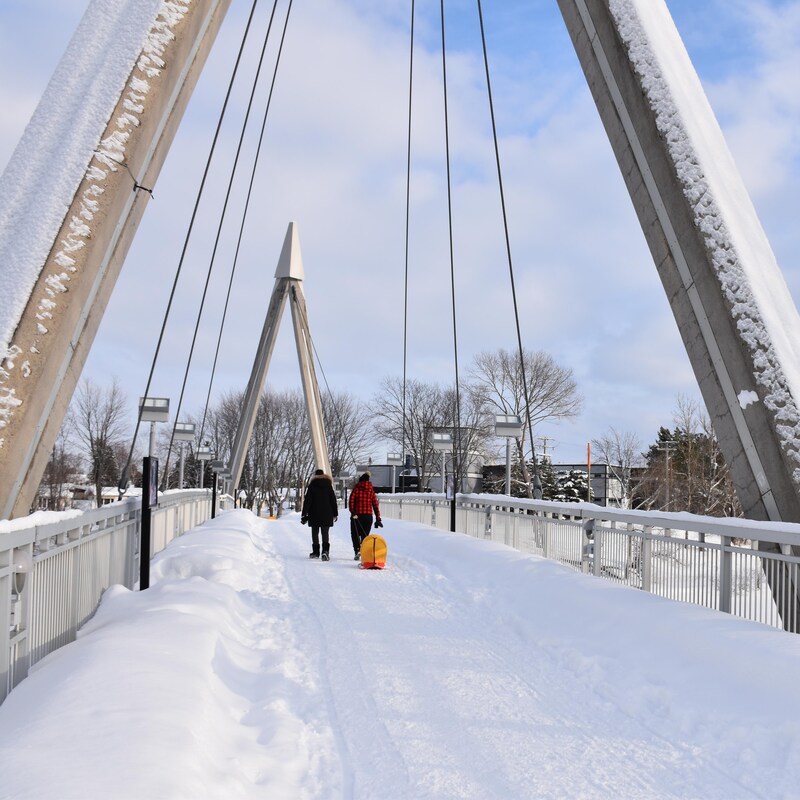 Des gens marchent sur la passerelle de la rivière aux Sables.