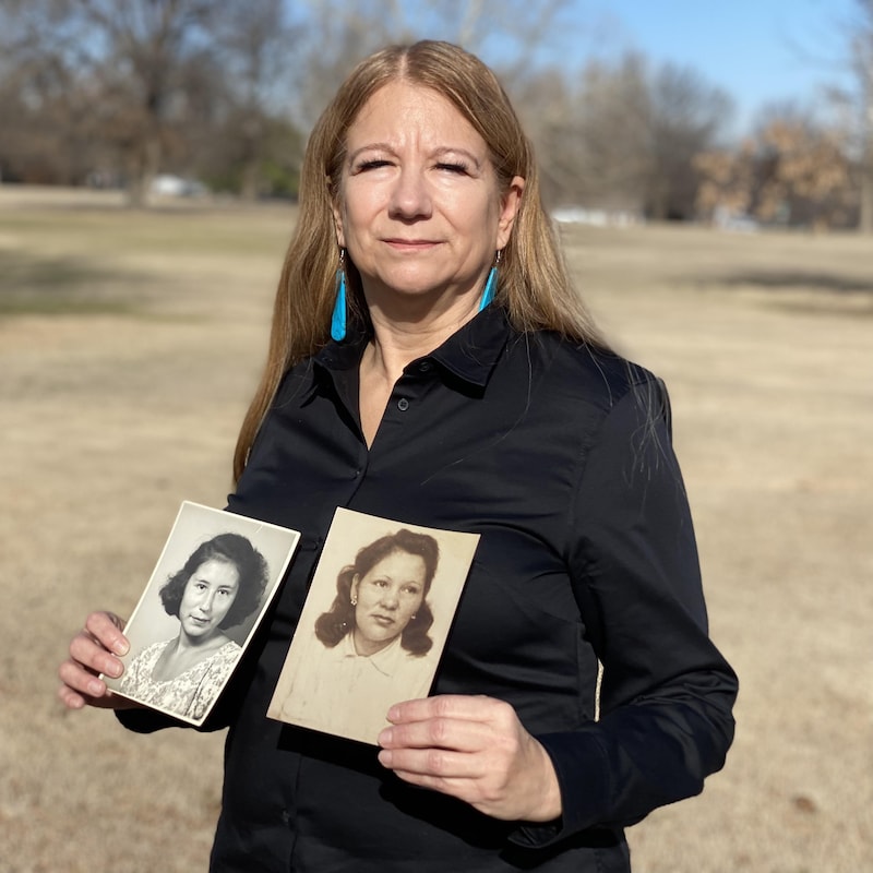Une femme porte dans les mains deux photos anciennes montrant des visages de femmes.