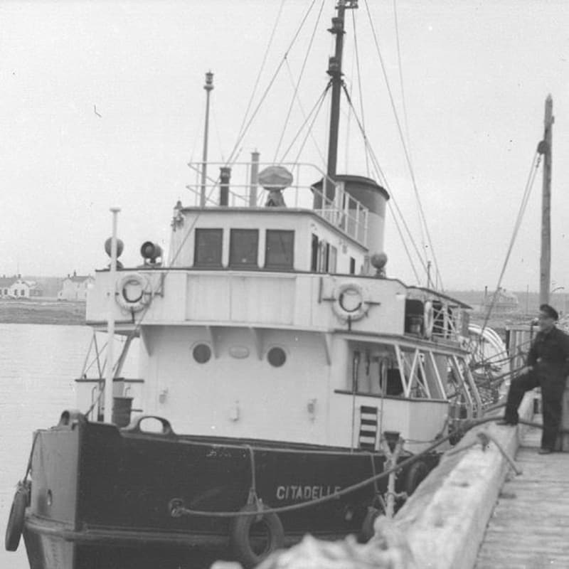Une photo d'archive illustre un capitaine, le pied sur le bord d'un petit bateau pilote à un quai.