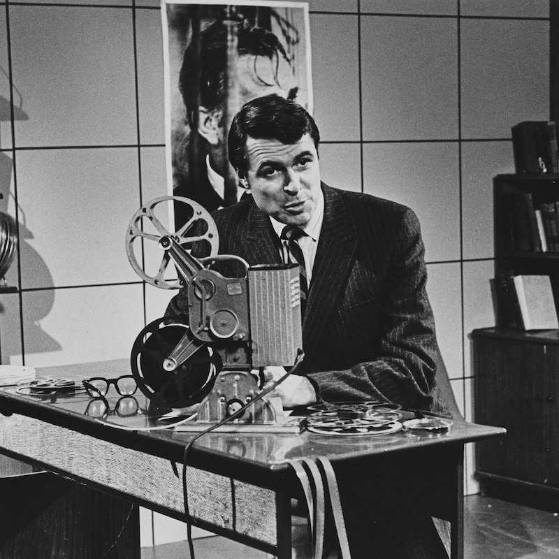 Dans un studio de télévision, l'animateur Richard Garneau manipule un projecteur de films.