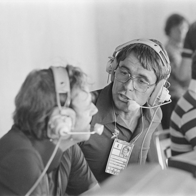 Jo Malléjac et Richard Garneau discutant assis devant leur ordinateur avec des casques-micros sur la tête.