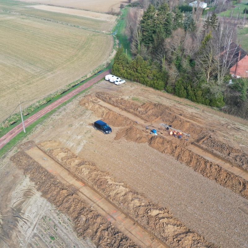 La vue aérienne montre des tranchées creusées dans un champ, où des archéologues sont à l'ouvrage.