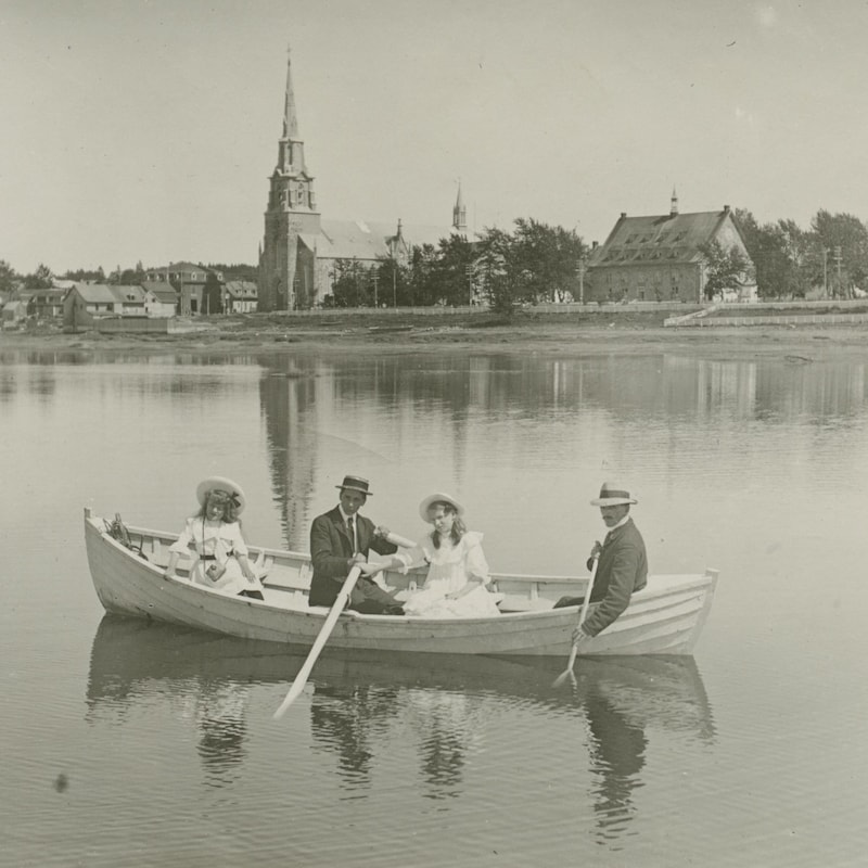 Image d'archive de deux hommes et deux femmes sur dans un canot sur le fleuve devant la ville de Rimouski.