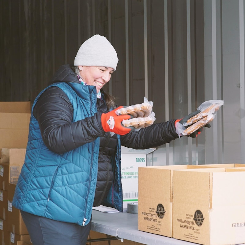 Dans un camion réfrigéré, une femme classe les paquets de saucisses dans des boîtes en souriant.