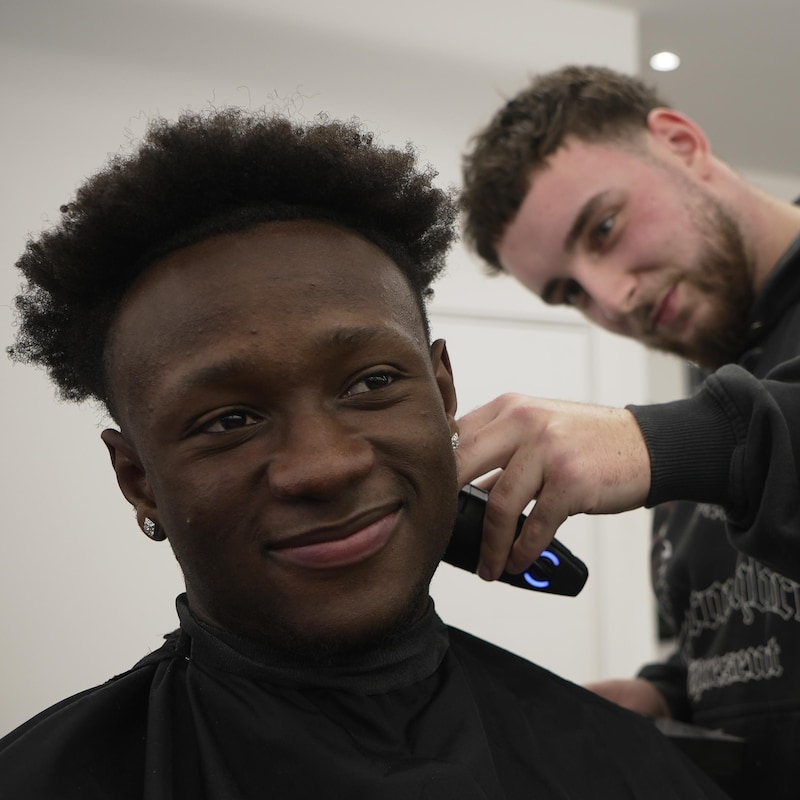 Il sourit pendant qu'on lui coupe les cheveux chez le barbier