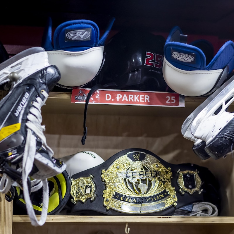 Des patins accrochés à un casier dans un vestiaire de hockey. On y voit aussi un casque et une ceinture de lutte.