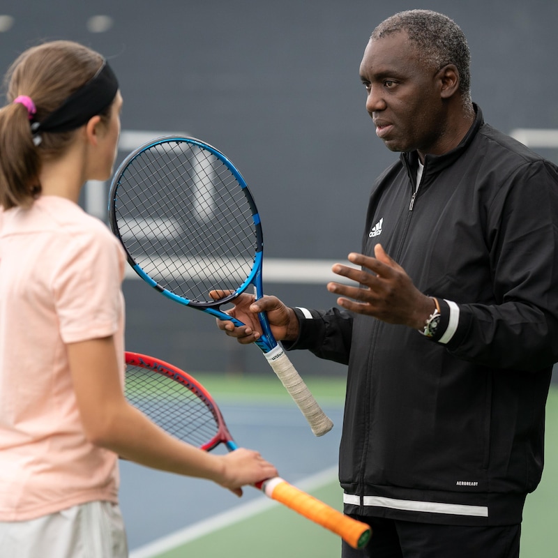 Un entraîneur de tennis parle à une joueuse près de terrain