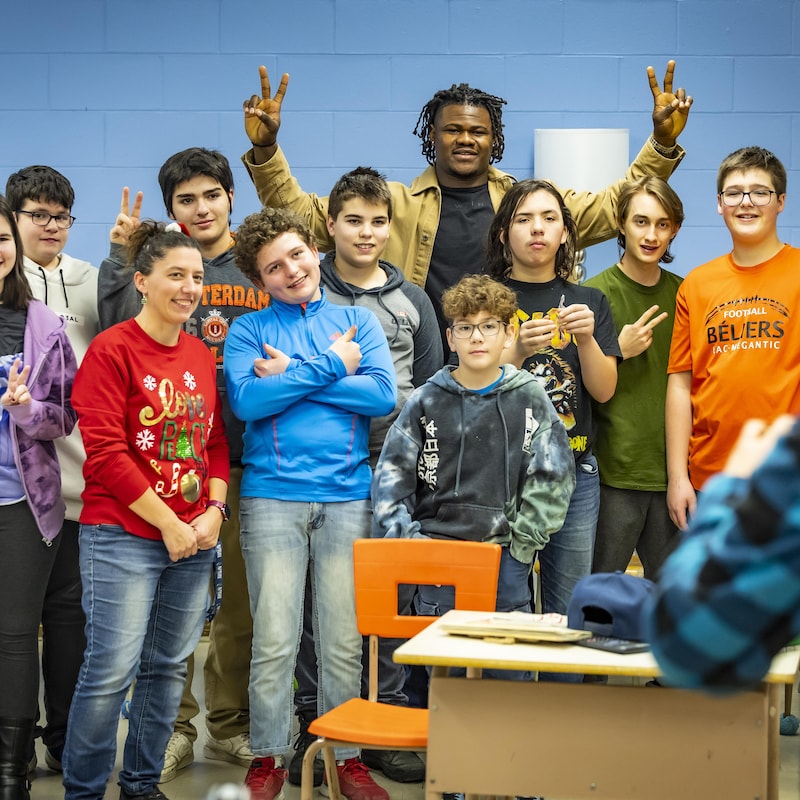 Des élèves dans une classe prennent une photo de groupe avec un homme qui fait des mains un signe de paix.
