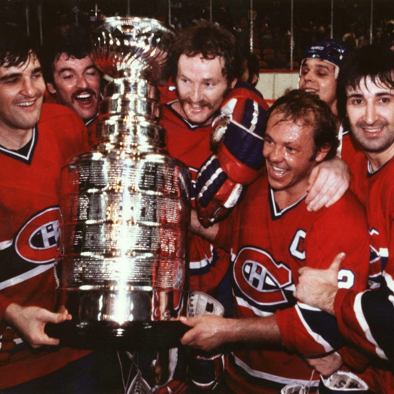 Des joueurs de hockey en rouge sourient autour d'un trophée qu'ils viennent de remporter.