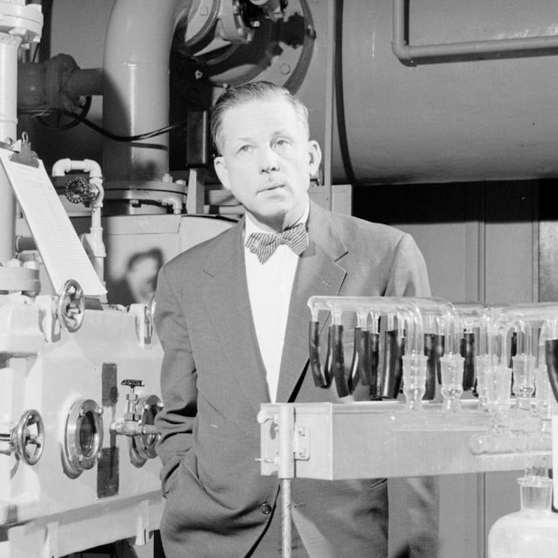 Le microbiologiste Armand Frappier se tient debout à côté d'équipements scientifiques.