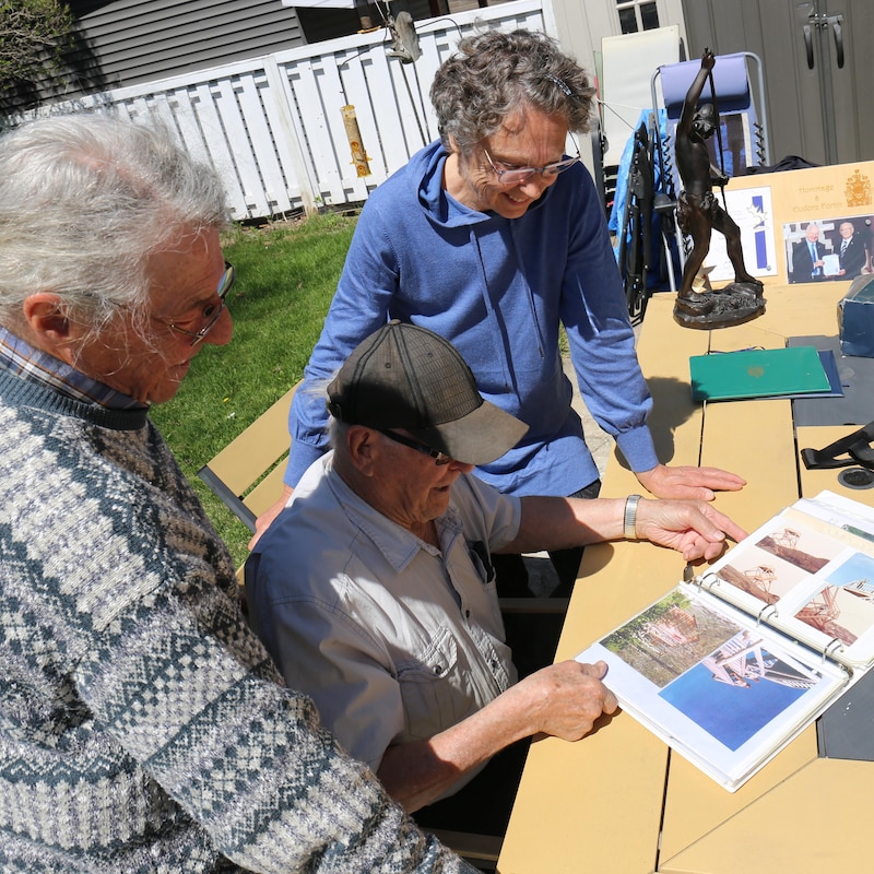 Charles Roberge, Eudore Fortin et Johanne Leduc regardent un album photo sur une table de picnic