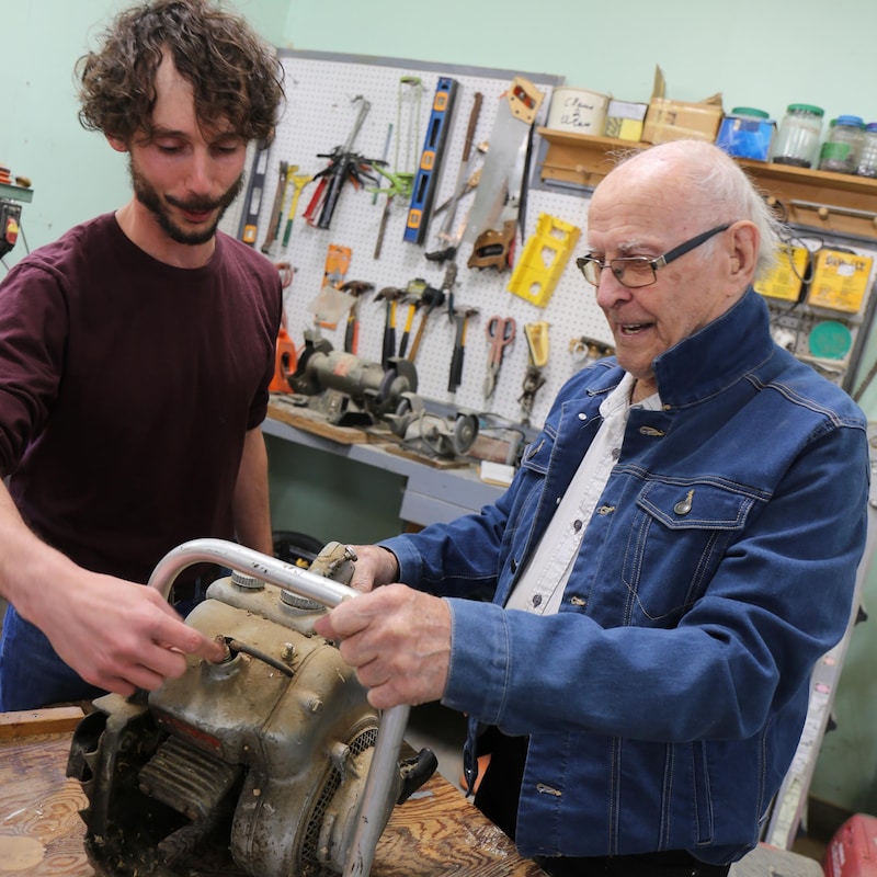 Justin Verville Alarie et Eudore Fortin travaillent sur une scie à chaîne dans un atelier.