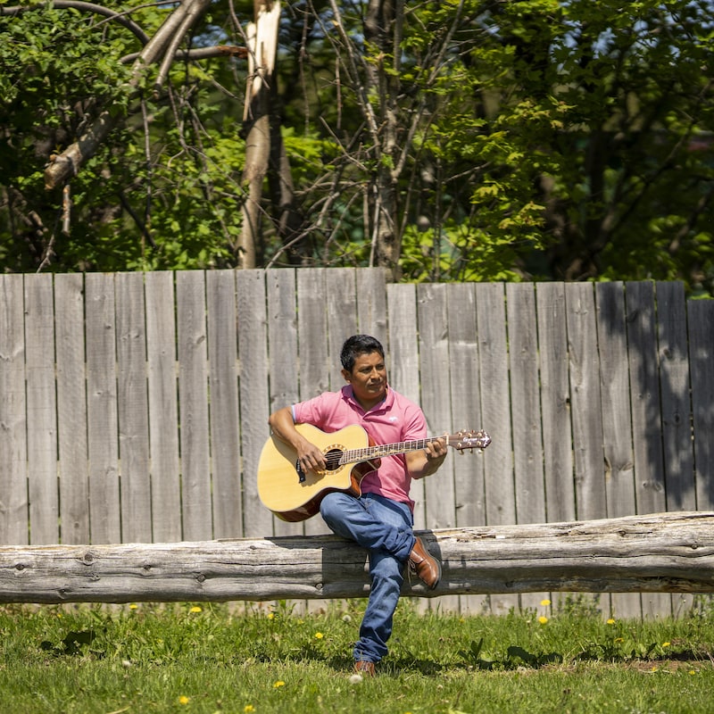 Un homme joue de la guitare sur un long tronc d'arbre.